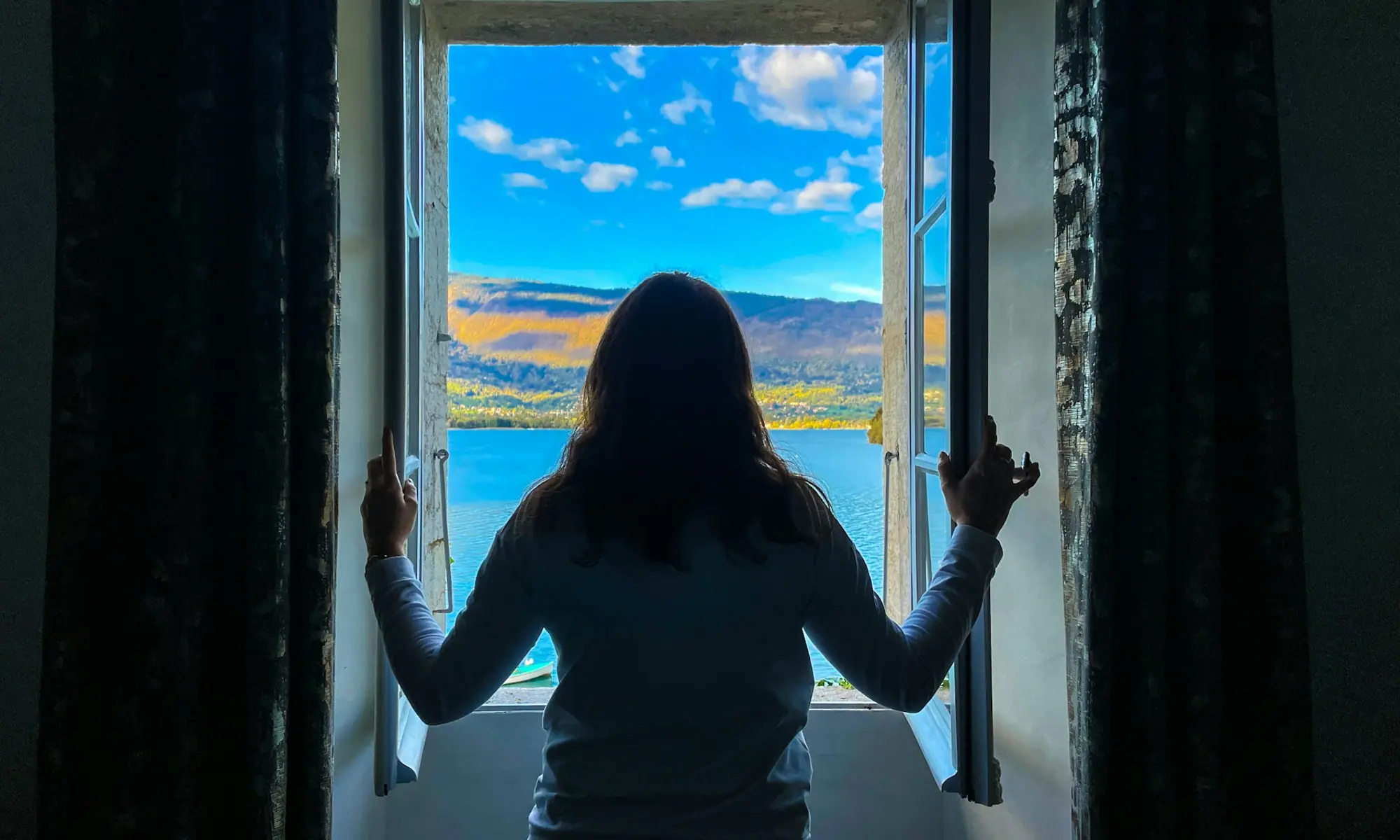 Woman opening a window onto a lake and hills — a clearer outlook with alcohol treatment in Modesto, CA